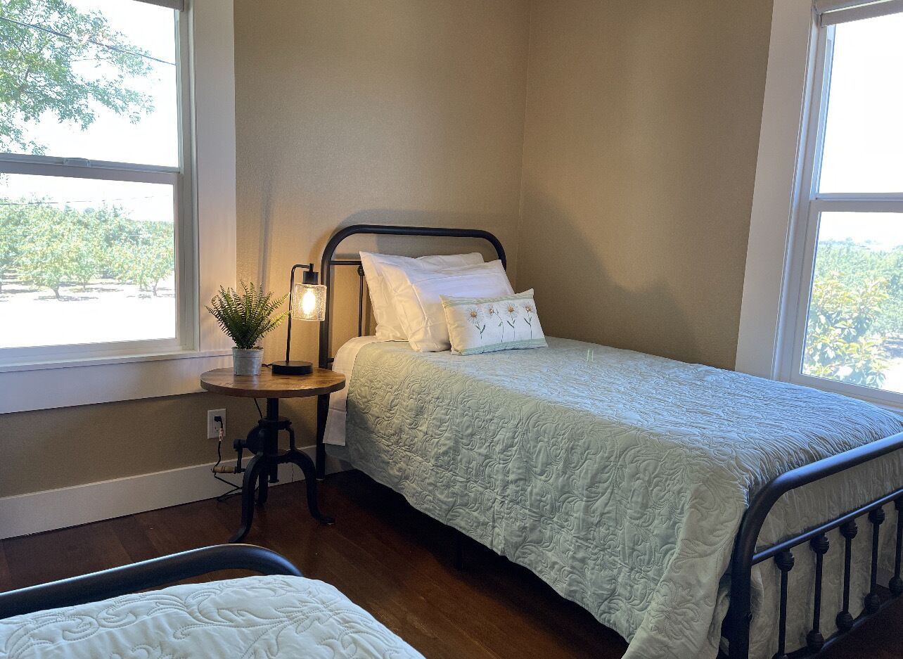 A bedroom with a bed, bedside table, lamp, and a view of greenery outside.