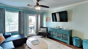 Una sala de estar con un sofá, una mesa de centro, un mueble color turquesa y un televisor montado en la pared.