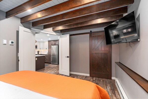 Un dormitorio con colcha naranja, techo de madera, puerta corredera y televisor montado.