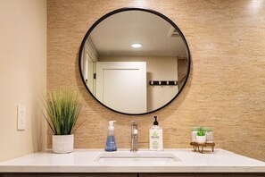 A bathroom with a round mirror, a sink, a potted plant, and toiletries.