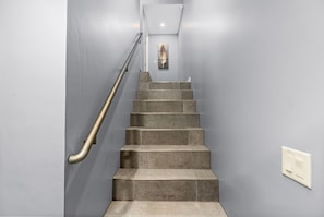 Una escalera con barandilla de metal, un interruptor de luz en la pared y una obra de arte enmarcada en la parte superior.