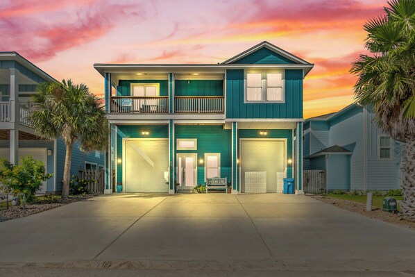 A two-story house with a balcony, garage doors, and a well-lit driveway. - Sun of a Beach by Silver Sands Vacation Rentals (Port Aransas)