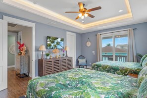 A bedroom with two beds, a ceiling fan, a large window, and a view of the outside.
