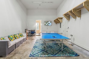 A room with a ping pong table, a sofa with floral cushions, and a patterned rug. - Sun of a Beach by Silver Sands Vacation Rentals (Port Aransas)