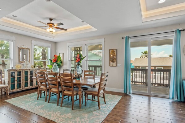 A dining area with a wooden table, chairs, and a ceiling fan. There is a sliding glass door leading to an outdoor area.