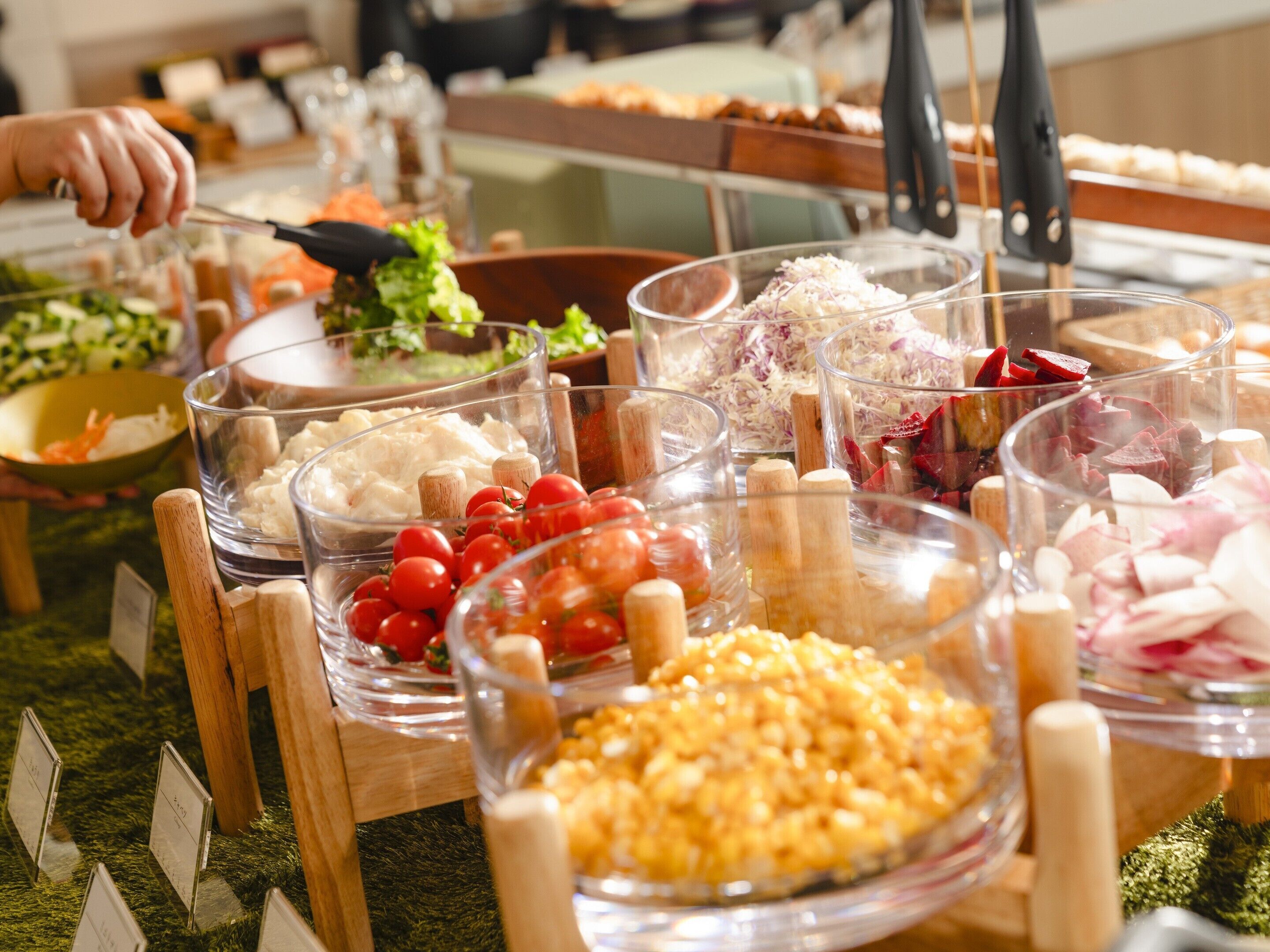 En buffet med forskellige madvarer i gennemsigtige skåle, herunder grøntsager, kød og korn.