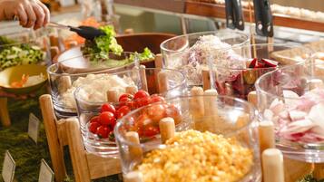 Un bufé con diversos alimentos en recipientes transparentes, como verduras, carnes y cereales.