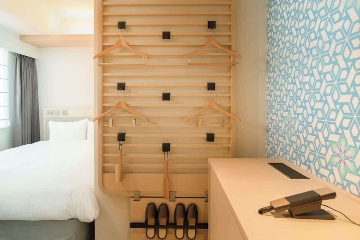 Habitación de hotel con cama, armario de madera con espacio para colgar, escritorio y silla, y pared con diseño.