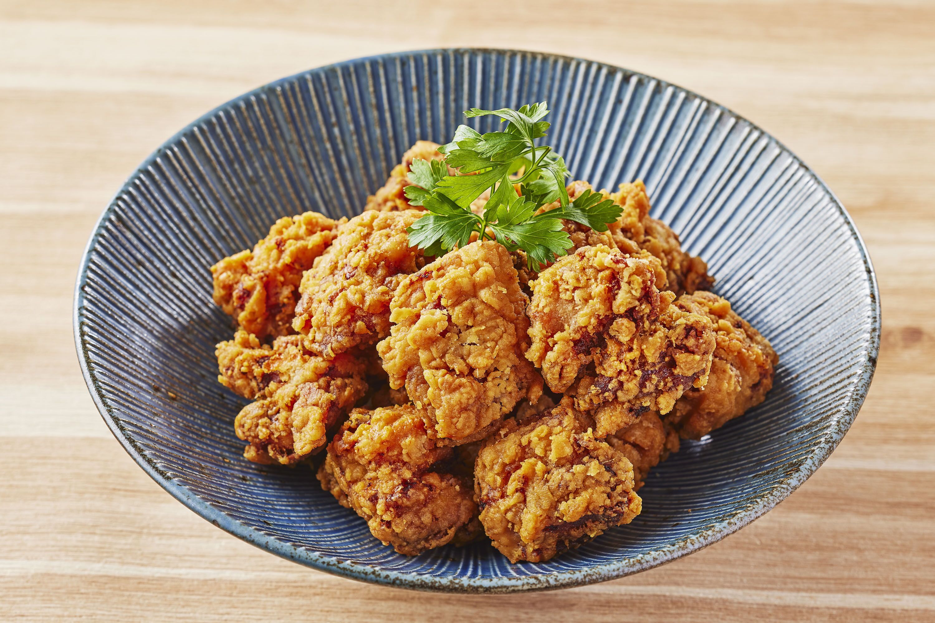 Un plato de pollo frito adornado con perejil sobre un plato de cerámica azul.