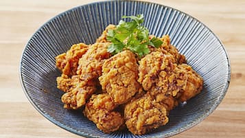 Un plato de pollo frito adornado con perejil sobre un plato de cerámica azul.