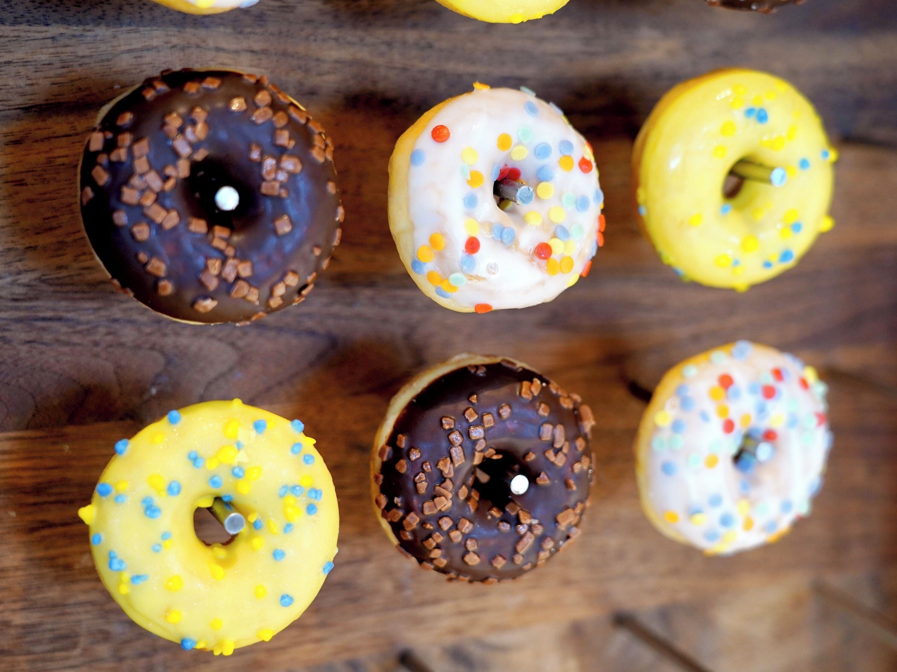 A top-down view of a wooden surface with six donuts arranged in two rows.