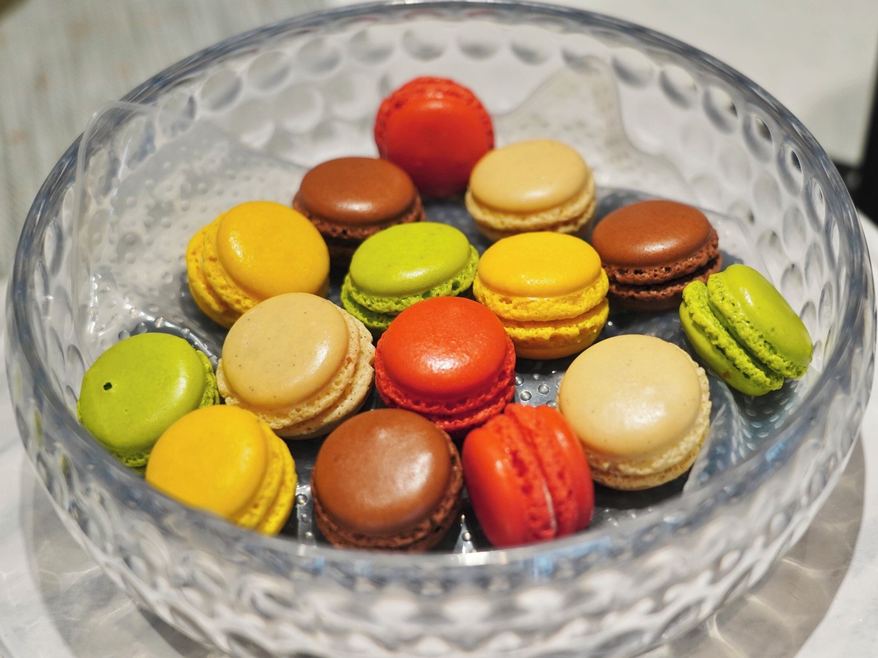 Un cuenco de vidrio transparente con macarons de varios colores.