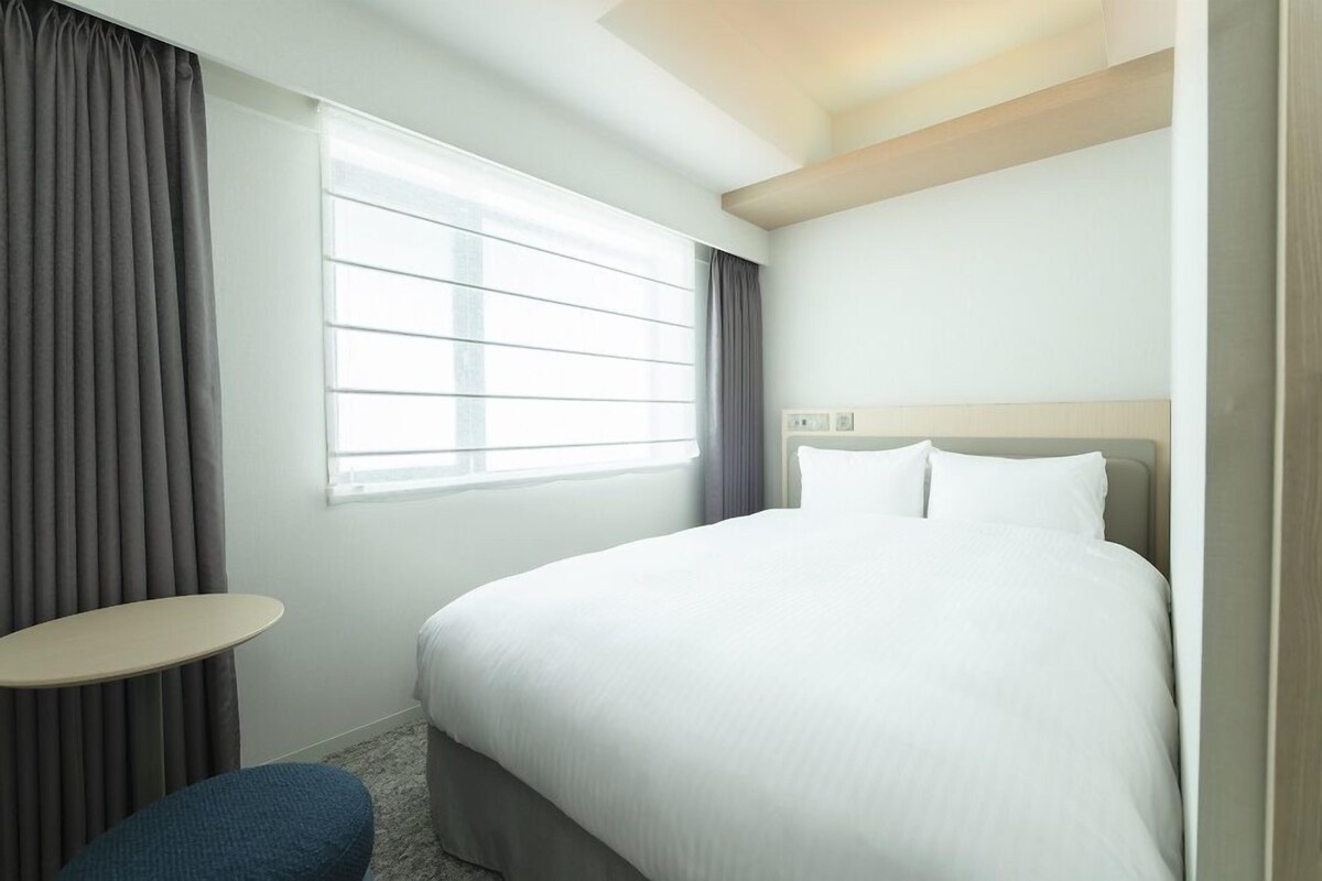 A hotel room with a large bed, a small round table, and a window with curtains.