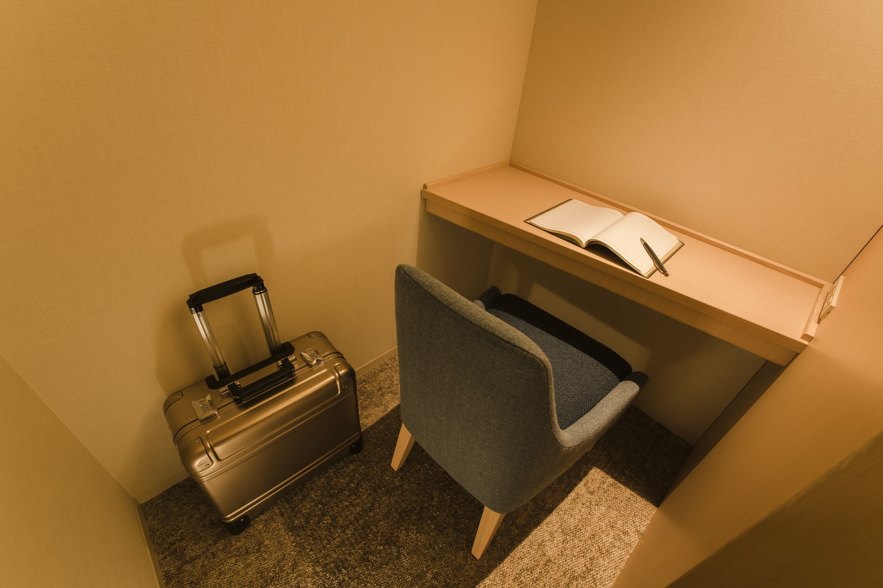 A small office space with a desk, a chair, a suitcase, and a book.