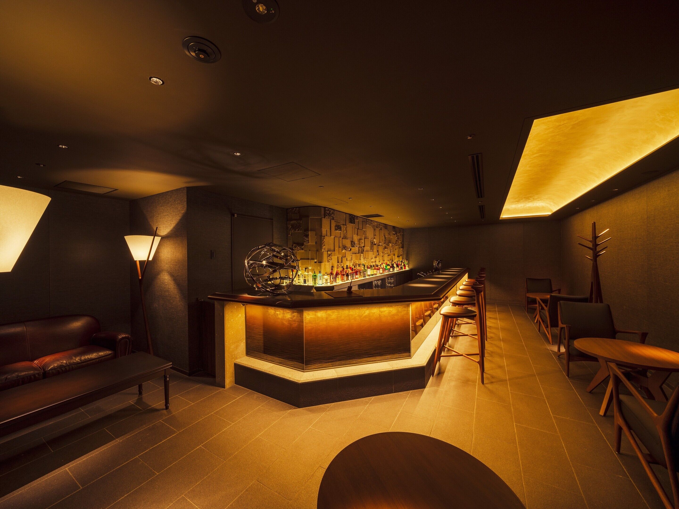 A bar area with a long counter, stools, and a seating area with a couch and chairs.