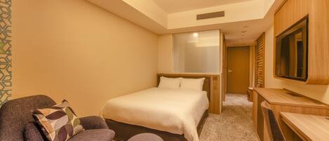Habitación de hotel con cama, zona de estar con sillón y reposapiés, escritorio y televisor.