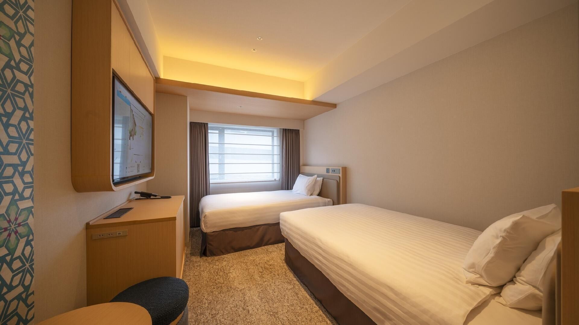 A hotel room with two beds, a desk, a television, and a window with curtains.