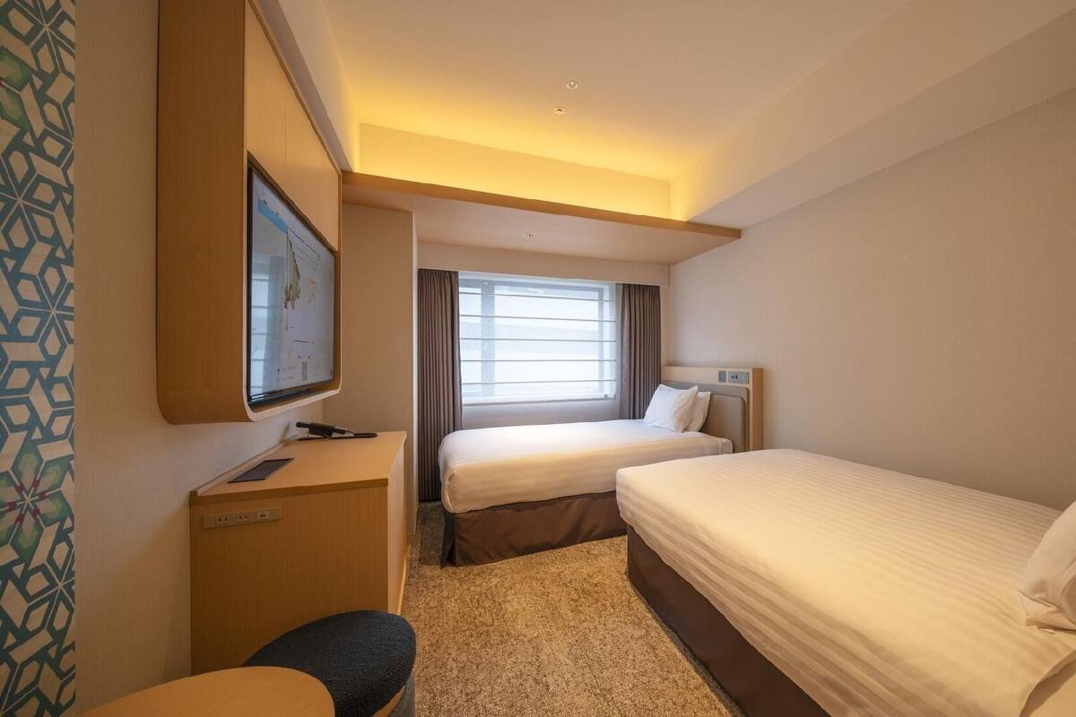 Une chambre d’hôtel avec deux lits, un bureau, une télévision et une fenêtre avec des rideaux.