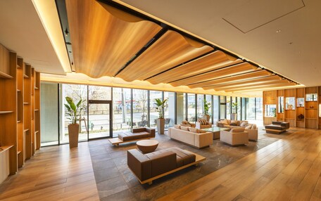 A spacious lobby with wooden flooring, multiple seating areas, and large windows offering views of the outside.