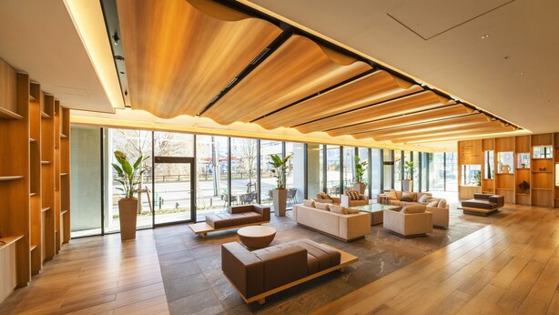 Un hall amplio con suelo de madera, varias zonas de estar y grandes ventanales con vistas al exterior.