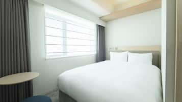 A hotel room with a large bed, a small table, and a window with curtains.