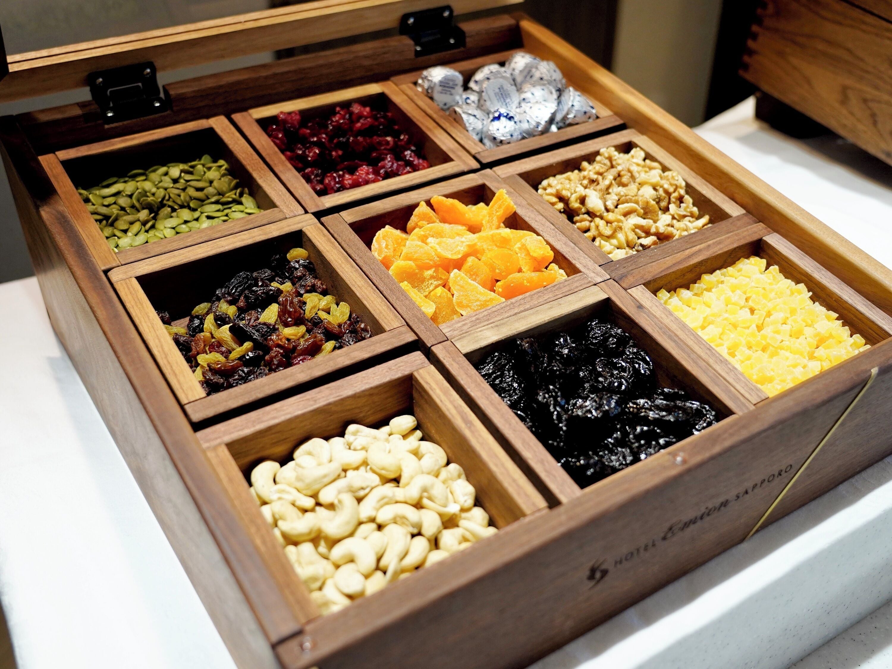 Une boîte en bois compartimentée contenant divers fruits secs et noix.