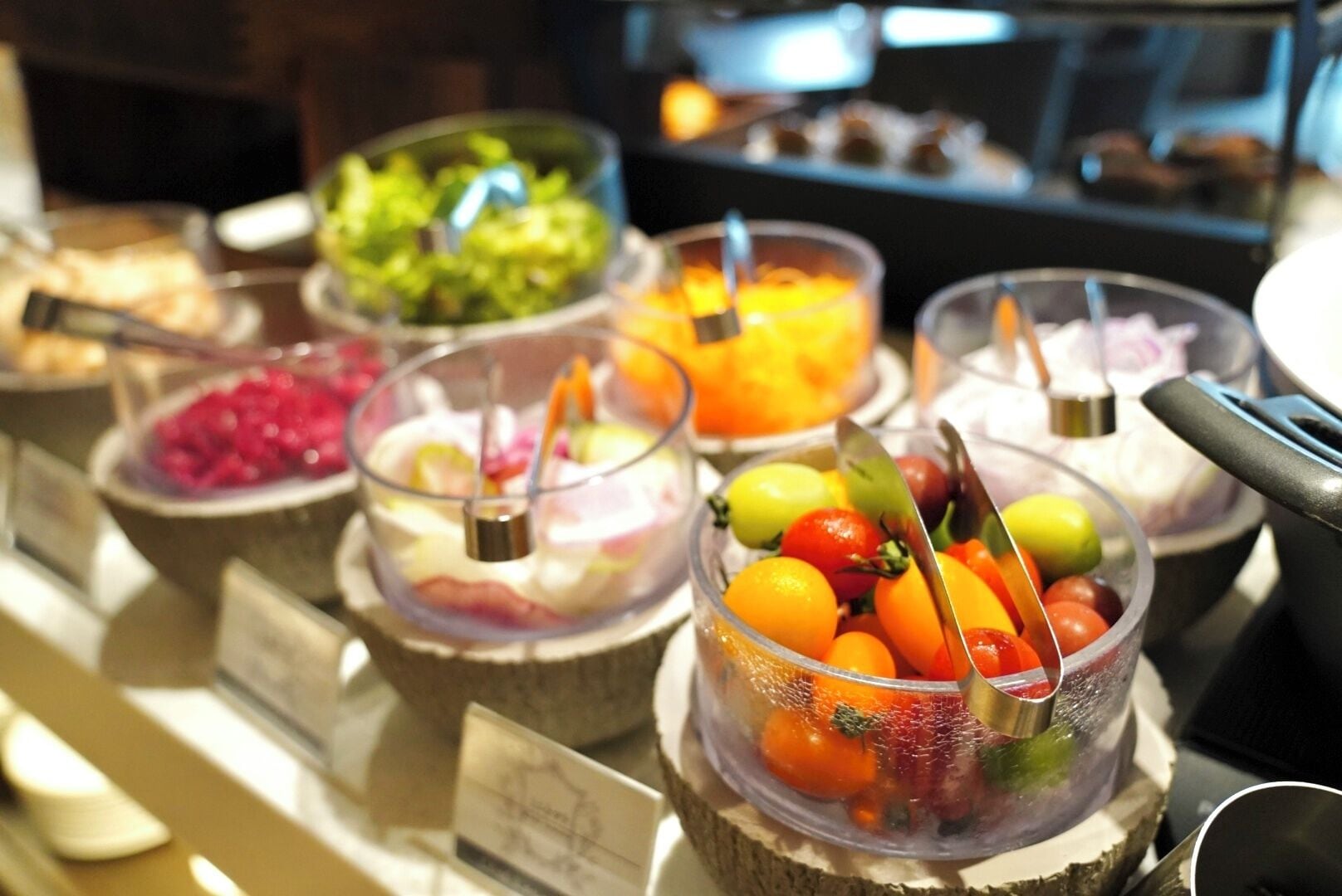 Un bufé con diversos alimentos presentados en recipientes transparentes.