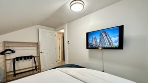 Une chambre d’hôtel avec un lit, un téléviseur fixé au mur, un porte-manteau et une porte donnant sur une autre pièce.