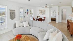 A modern living room with a curved grey sofa, a wooden coffee table, and a ceiling fan. - Seagull Sands by Ryson Vacation Rentals (Galveston)