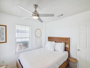 A bedroom with a bed, a ceiling fan, a window with blinds, a dreamcatcher, and a framed picture on the wall. - Seagull Sands by Ryson Vacation Rentals (Galveston)