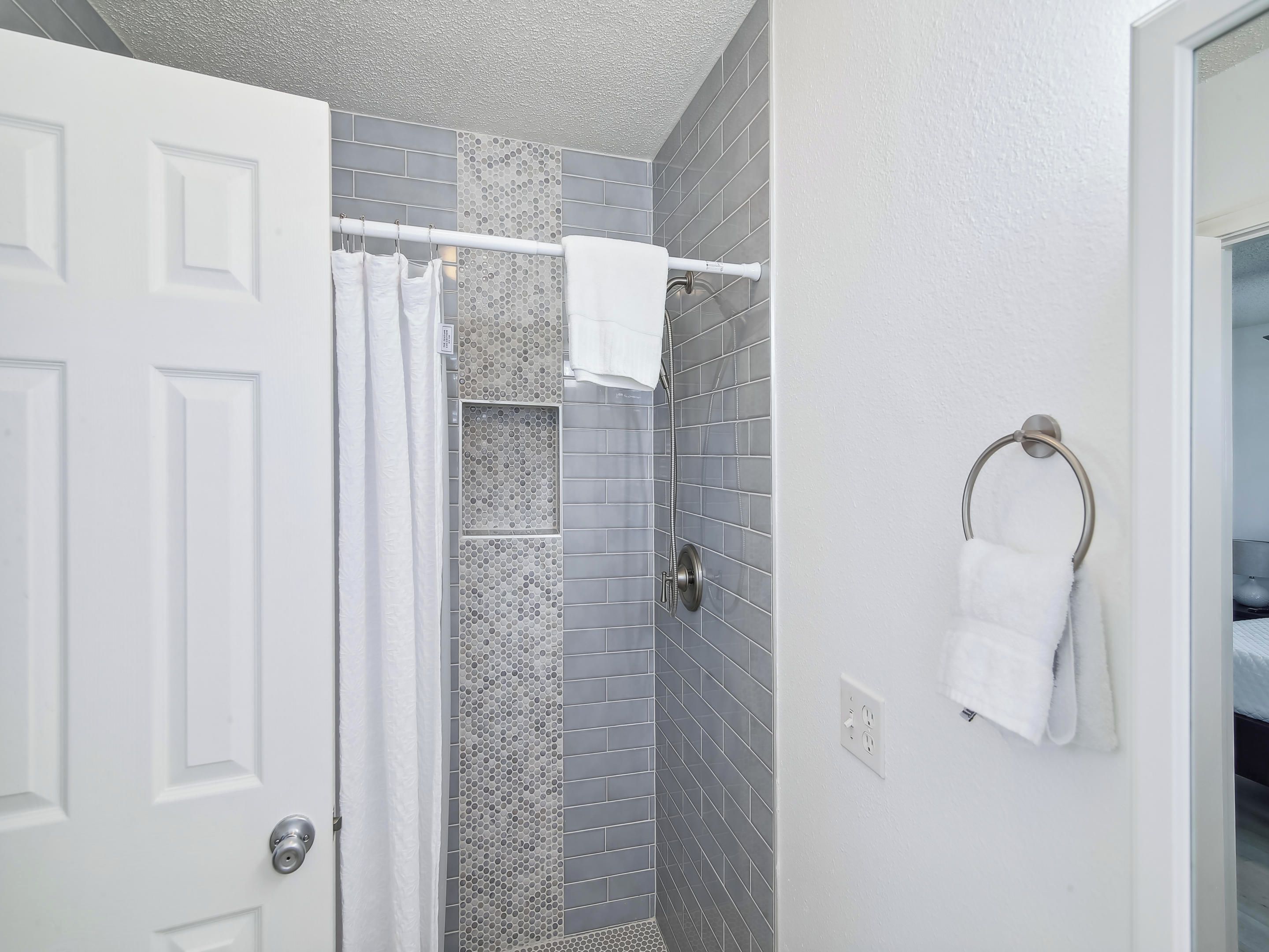 Un baño con ducha, paredes de azulejos, un perchero y una puerta.