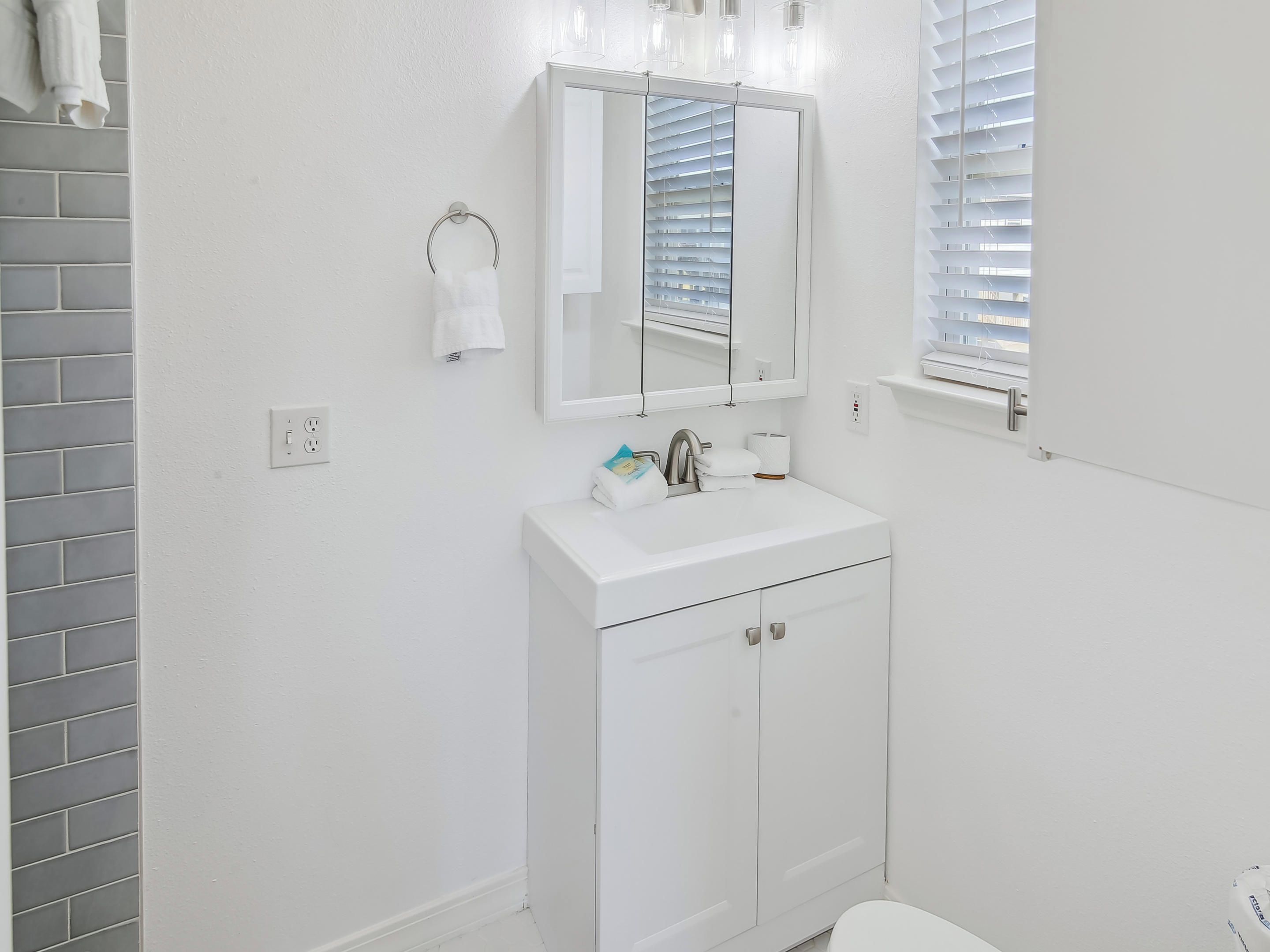 A white bathroom with a tiled shower wall, a white sink with a mirror above it, and a toilet.