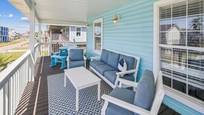 A covered porch with a blue exterior, white railings, and a patterned floor. - Seagull Sands by Ryson Vacation Rentals (Galveston)