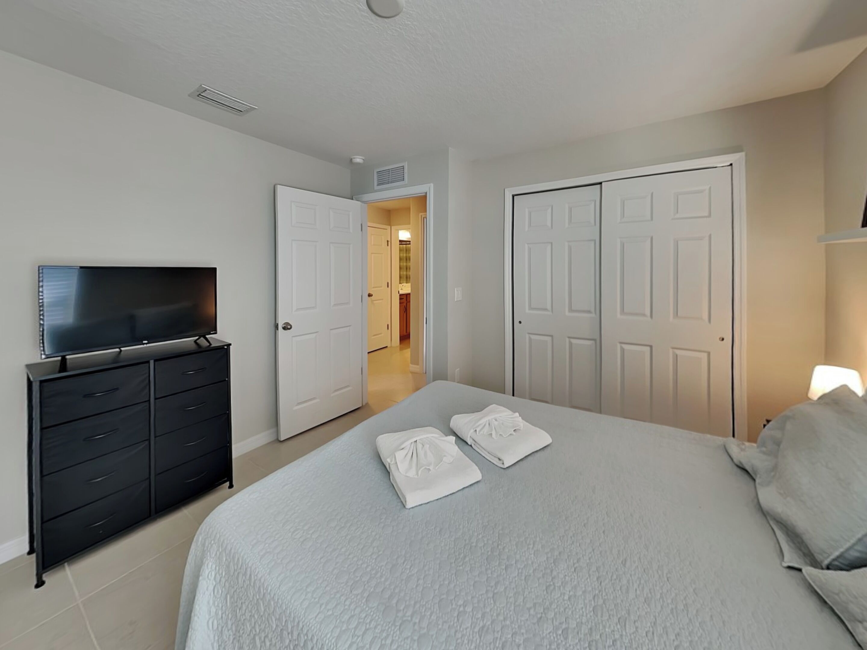 Une chambre à coucher avec un lit, un téléviseur posé sur une commode et deux portes donnant sur d’autres pièces.