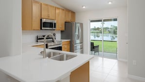 Una cocina moderna con armarios de madera, electrodomésticos de acero inoxidable y un amplio ventanal con vistas a una zona verde.
