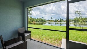 Un balcón con mobiliario de mimbre con vistas a un lago y follaje.