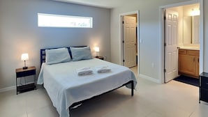 Un dormitorio moderno con una cama, dos mesitas de noche, una lámpara de pared y una puerta que da a un baño.