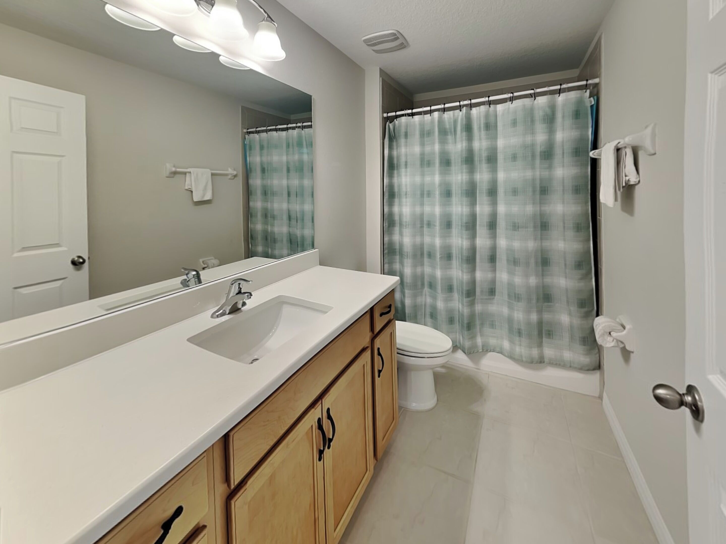 Un baño con un lavamanos blanco, armarios de madera, inodoro y cortina de ducha.