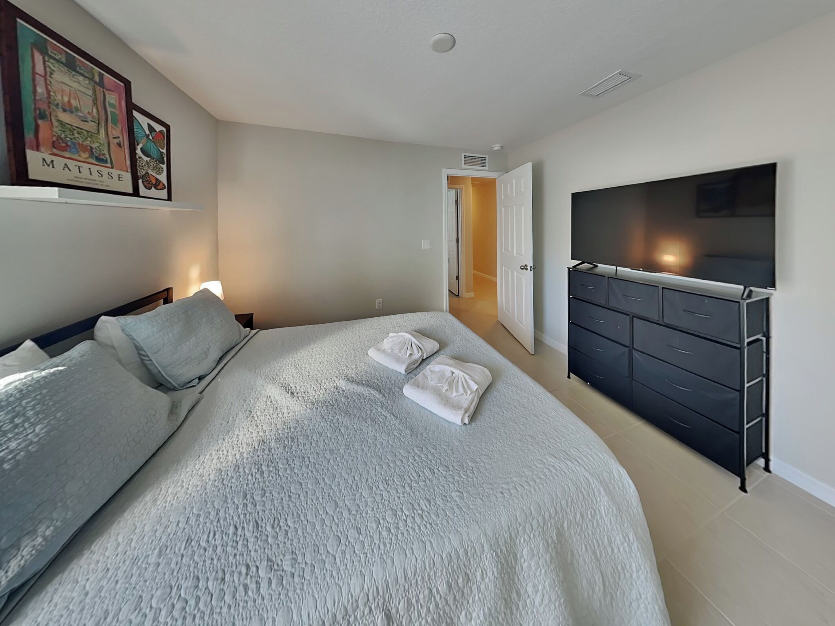 Een slaapkamer met een bed, een dressoir, een televisie en een deur naar een andere kamer.
