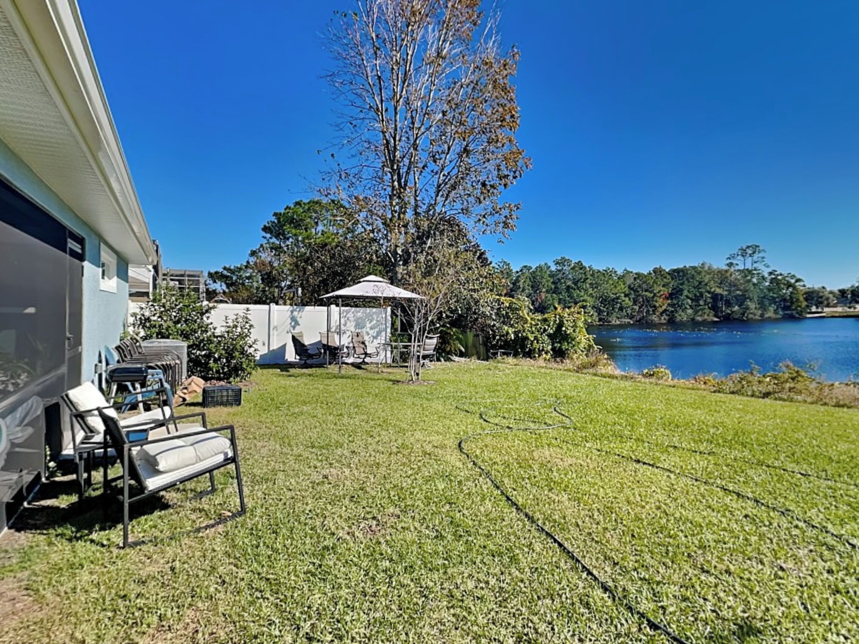 A grassy backyard with a patio area, a covered seating area, and a view of a lake.