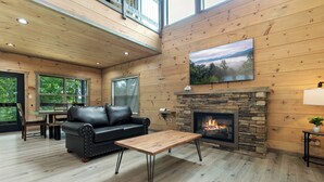 Un salon chaleureux avec une cheminée en pierre, des murs en bois, un canapé en cuir noir et une table basse en bois.