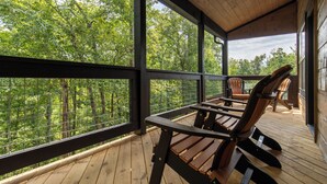 Une terrasse en bois offrant une vue sur une forêt, avec une table et deux chaises.