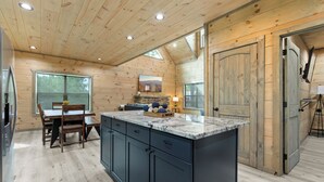 Une cuisine moderne avec des murs en bois, un grand îlot central et un coin repas comprenant une table et des chaises.