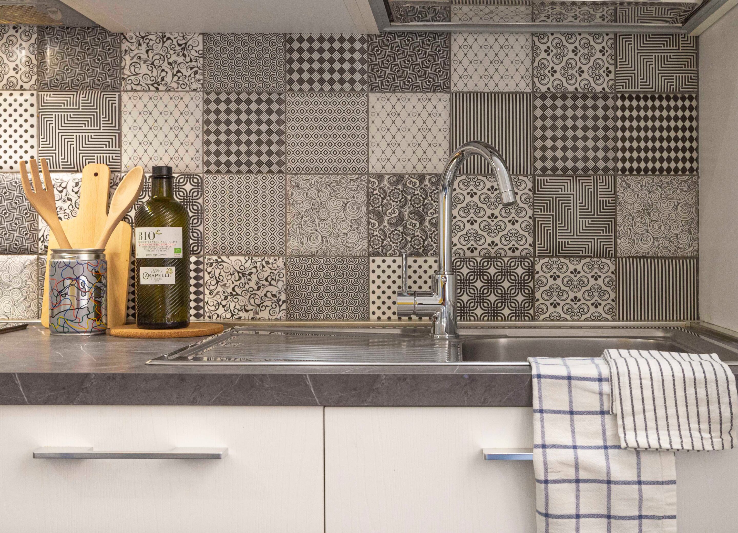 A kitchen with a patterned backsplash, a stainless steel sink, and wooden utensils.