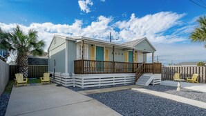 A single-story building with a porch, a small table, and two Adirondack chairs. - Tranquil Cove by Jackson Mountain Rentals (Port Aransas)