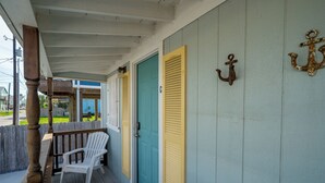 A covered porch with a wooden bench, a turquoise door, and a white door with a yellow shutter. - Tranquil Cove by Jackson Mountain Rentals (Port Aransas)