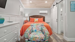 A bedroom with a bed, a chair, a dresser, a TV, an air conditioner, and a sign on the wall. - Tranquil Cove by Jackson Mountain Rentals (Port Aransas)