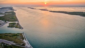 An aerial view of a coastal area with a body of water, land with vegetation, and a clear sky. - Tranquil Cove by Jackson Mountain Rentals (Port Aransas)