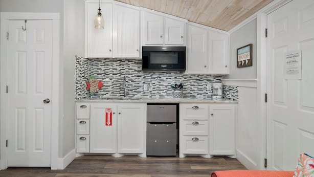 A kitchen with white cabinets, a microwave, a refrigerator, and a tiled backsplash. - Tranquil Cove by Jackson Mountain Rentals (Port Aransas)