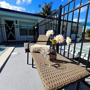 Relax in a serene outdoor seating area with a pool view, featuring two lounge chairs and a small table.